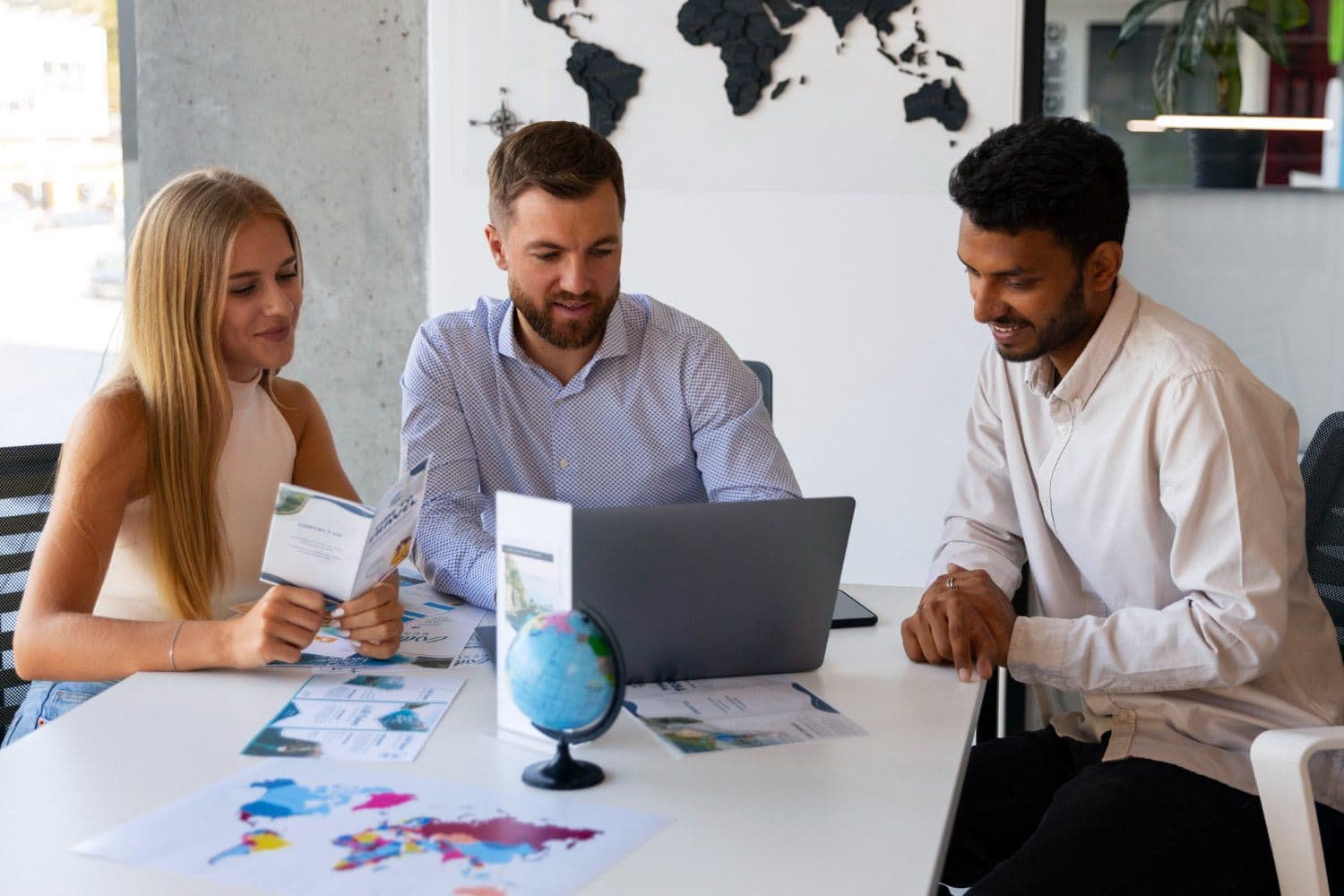Three colleagues collaborating with a laptop and globe in a bright office