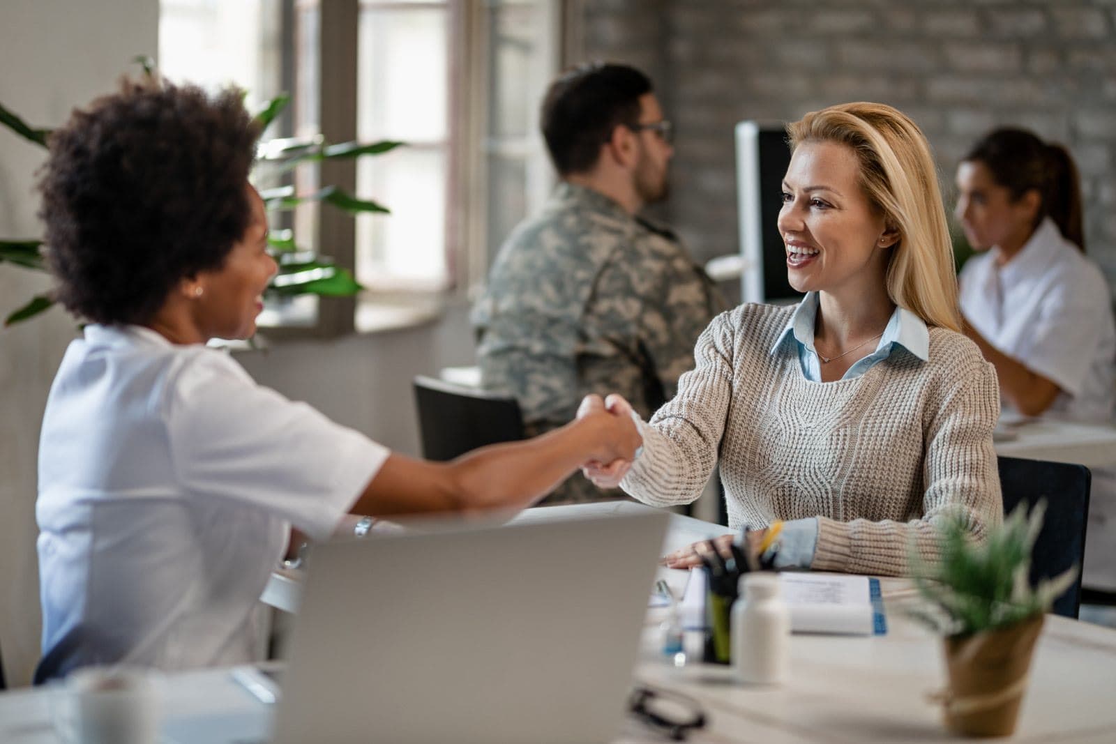 Two people shaking hands and smiling across a desk